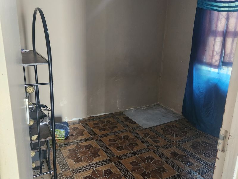 A small bedroom featuring patterned ceramic floor tiles and a window with a curtain rail, currently in need of cosmetic updates and wall repairs.