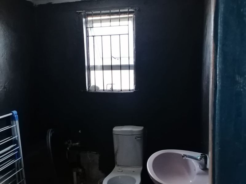 A small bathroom featuring a pedestal basin and toilet, with security bars on the window and a textured ceiling finish.
