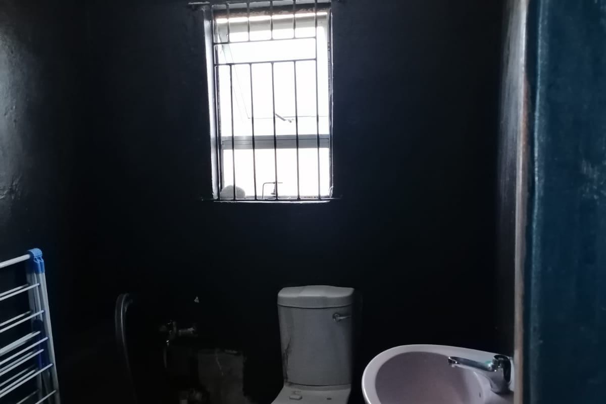 A small bathroom featuring a pedestal basin and toilet, with security bars on the window and a textured ceiling finish.