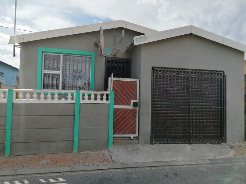 Front elevation of a single-story house featuring a concrete boundary wall, security gates, and a driveway entrance.