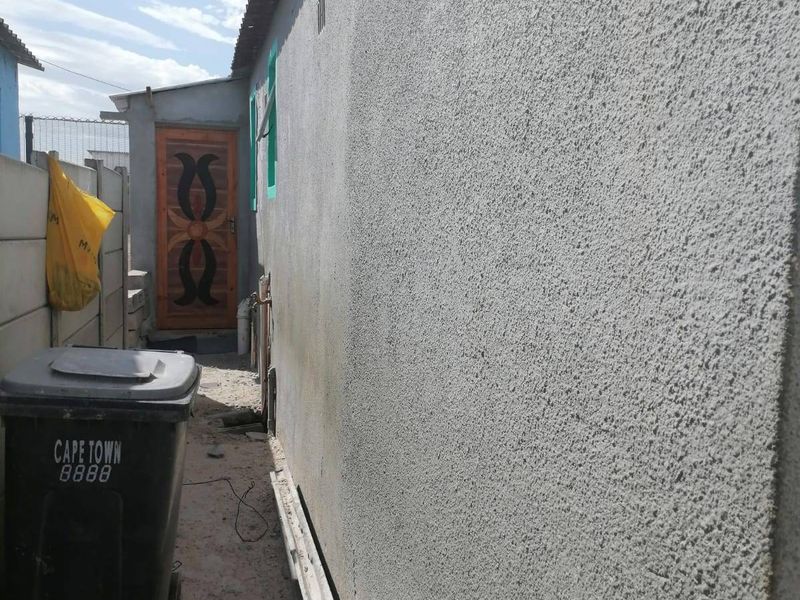A side exterior view of the property showing a textured wall finish, corrugated roof, and a timber door leading to the rear area.