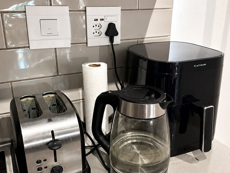 A close-up view of a modern kitchen countertop featuring a neutral subway tile backsplash, stone-look surface, and integrated electrical outlets.