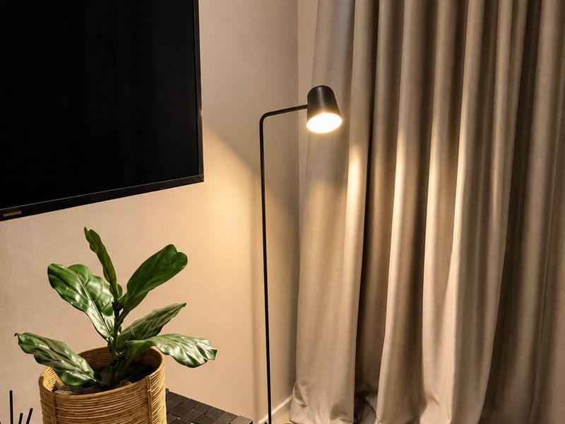 A modern living room corner featuring a wall-mounted television, floor lamp, and floor-to-ceiling curtains.