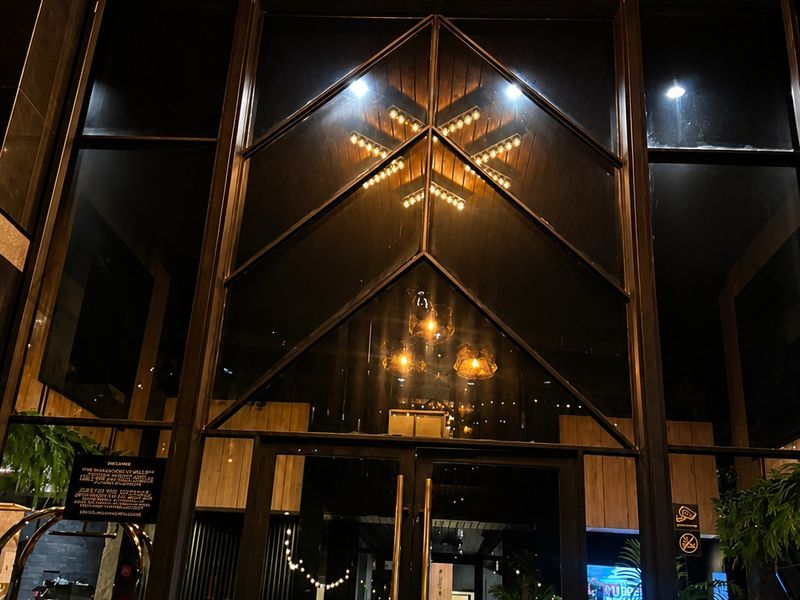 Modern apartment building entrance featuring a striking timber-clad ceiling, expansive glass facade, and contemporary metal-framed doors with integrated lighting.