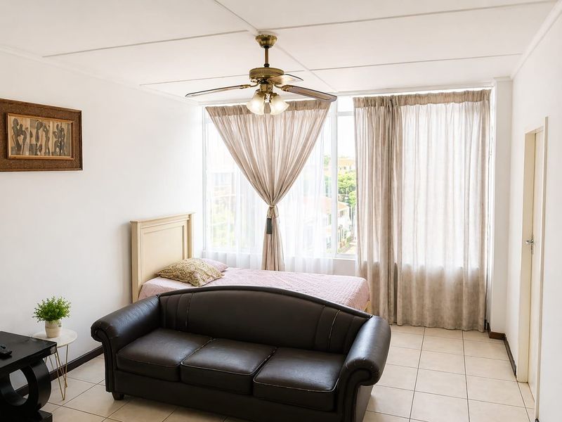 A bedroom featuring tiled flooring, a ceiling fan, and a large window that allows for ample natural light.
