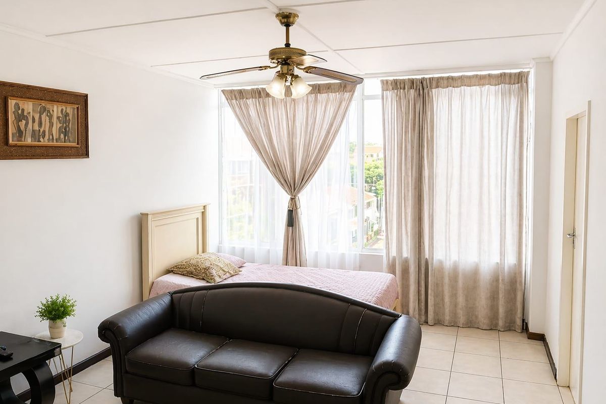 A bedroom featuring tiled flooring, a ceiling fan, and a large window that allows for ample natural light.