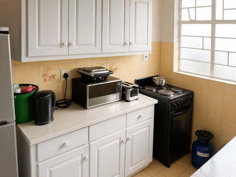 A functional kitchen featuring white cabinetry, tiled backsplash, and a freestanding stove, offering a practical layout with natural light from the window.