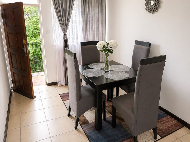 A bright dining area featuring tiled flooring and direct access to an outdoor balcony through a wooden door.