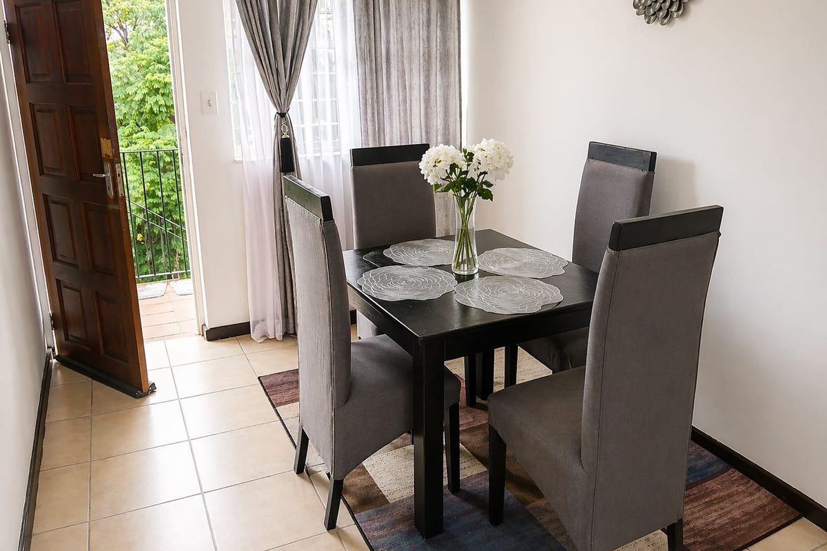 A bright dining area featuring tiled flooring and direct access to an outdoor balcony through a wooden door.