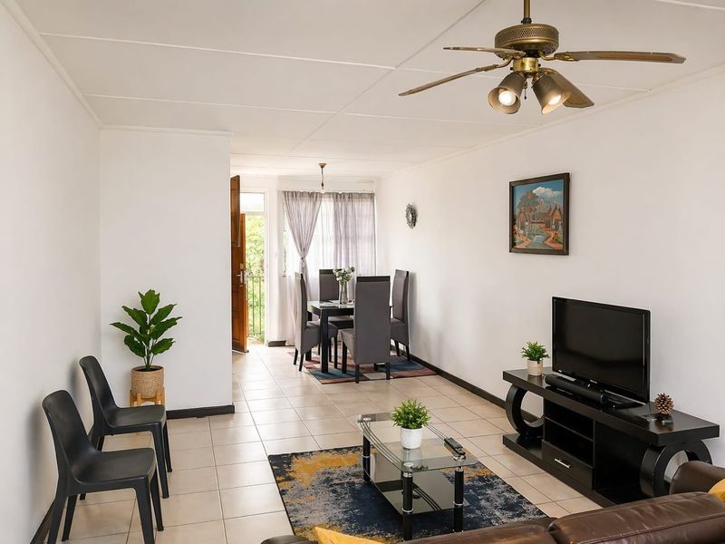 Open-plan living and dining area featuring neutral tiled flooring, a ceiling fan, and direct access to an outdoor balcony.