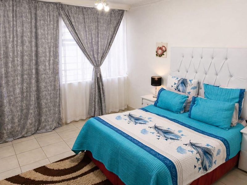 A well-maintained bedroom featuring tiled flooring and a large window with security bars, providing natural light to the space.