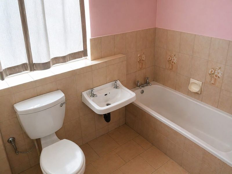 A functional bathroom featuring a ceramic bathtub, wall-mounted washbasin, and toilet, finished with neutral wall and floor tiling.