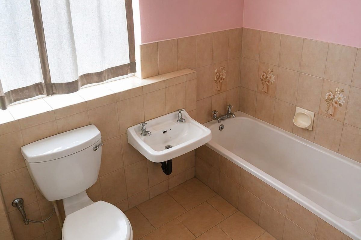 A functional bathroom featuring a ceramic bathtub, wall-mounted washbasin, and toilet, finished with neutral wall and floor tiling.