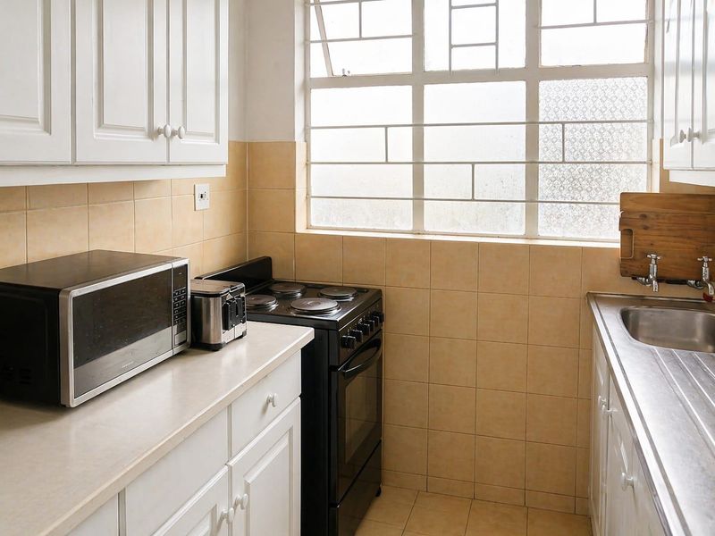 A functional kitchen featuring white cabinetry, laminate countertops, a stainless steel sink, and a freestanding electric stove with tiled backsplash.