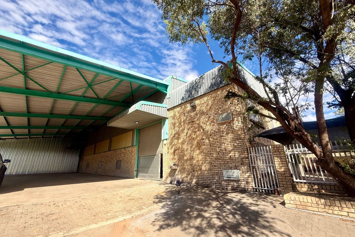 Commercial warehouse exterior featuring a large covered loading area, brick facade, roller shutter door, and secure perimeter fencing.