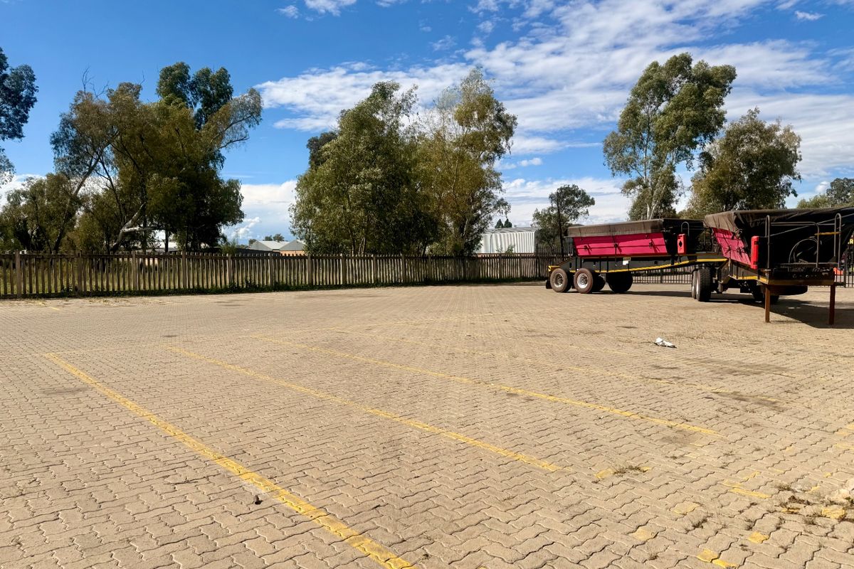 A spacious paved commercial parking area featuring perimeter fencing and clearly marked parking bays, suitable for vehicle storage or customer parking.