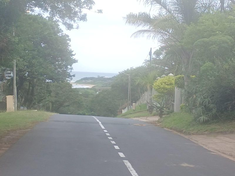 A street view showing the approach to the property with a distant view of the coastline and surrounding vegetation.