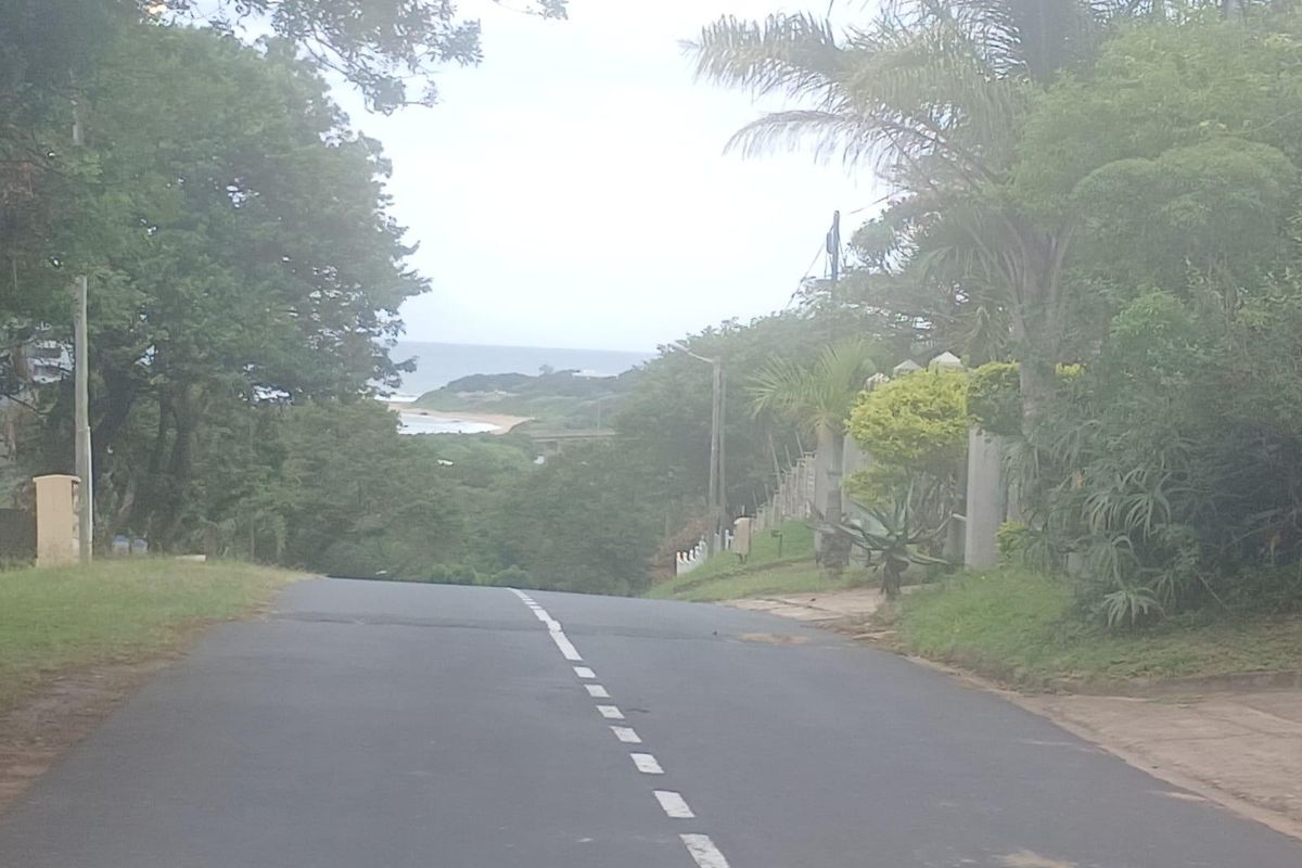 A street view showing the approach to the property with a distant view of the coastline and surrounding vegetation.