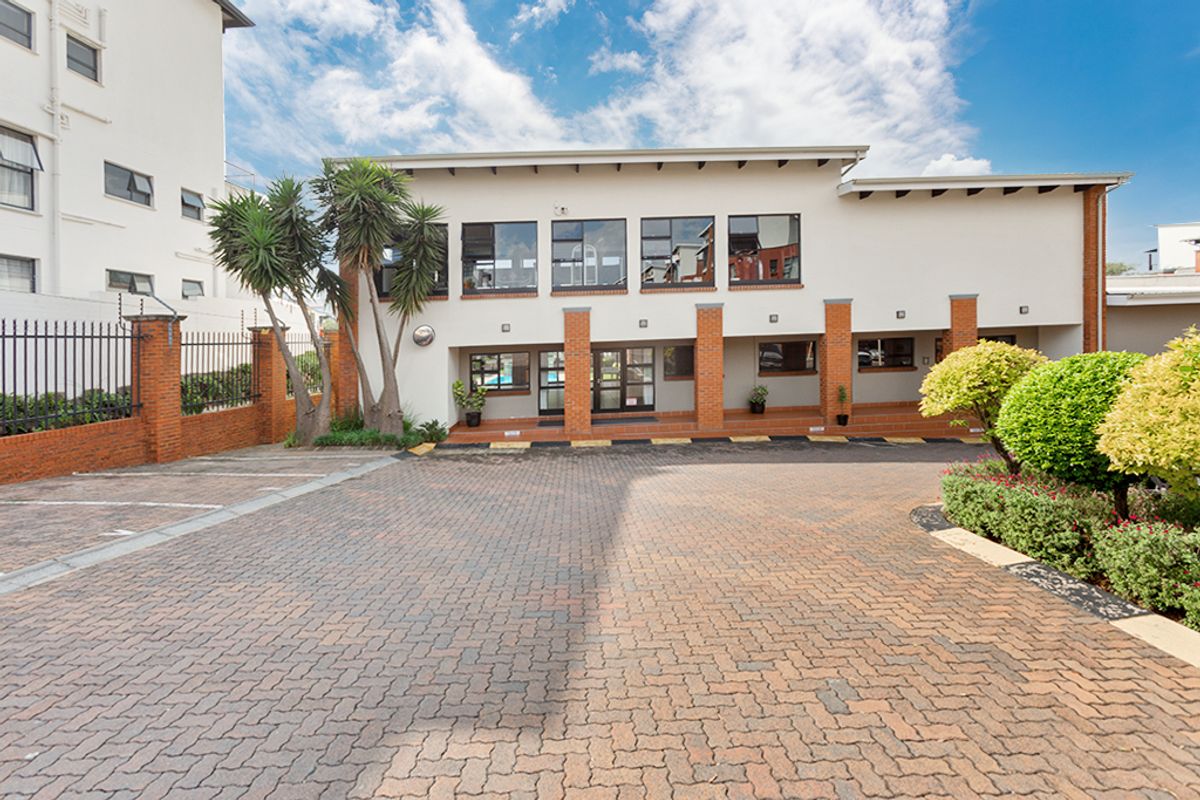 Front exterior view of the apartment complex featuring a paved driveway, brick pillar accents, and secure perimeter fencing.