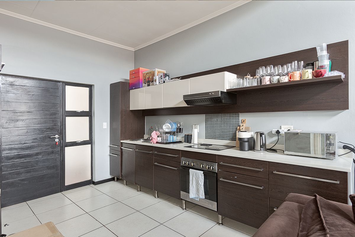 Modern kitchen featuring dark wood cabinetry, integrated oven and hob, mosaic splashback, and tiled flooring, offering a functional and contemporary cooking space.