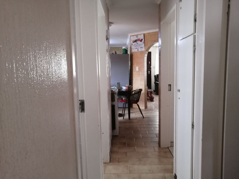 A view through a residential hallway featuring tiled flooring and built-in storage cupboards, leading towards an open-plan living area.