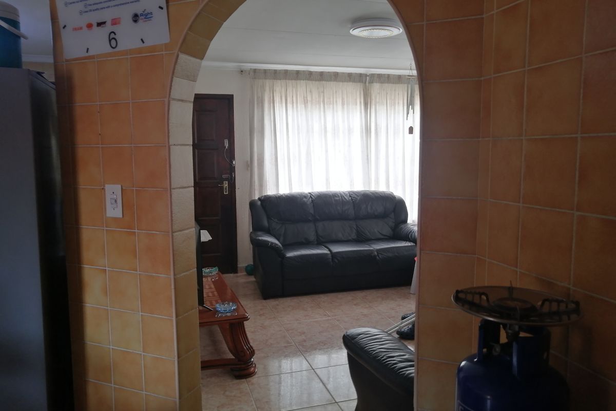 A living room viewed through a tiled archway, featuring tiled flooring and natural light from a window with curtains.