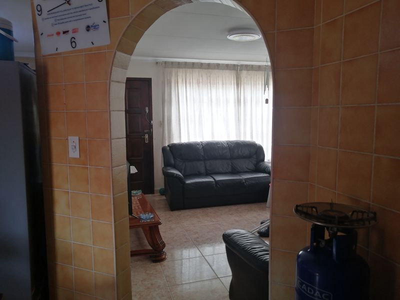 A living room viewed through a tiled archway, featuring tiled flooring and natural light from a window with curtains.