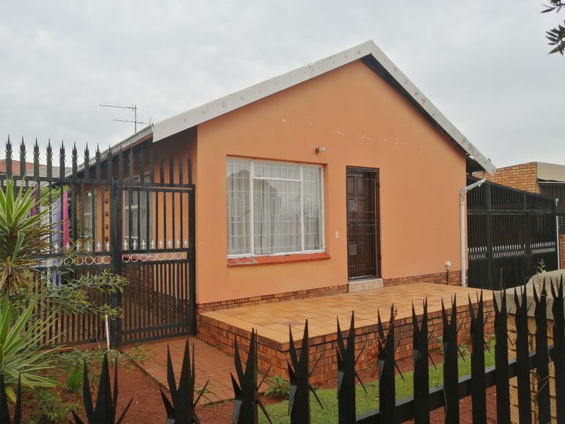 Front elevation of a detached house featuring a tiled porch, metal security fencing, and security gates on the main entrance and windows.