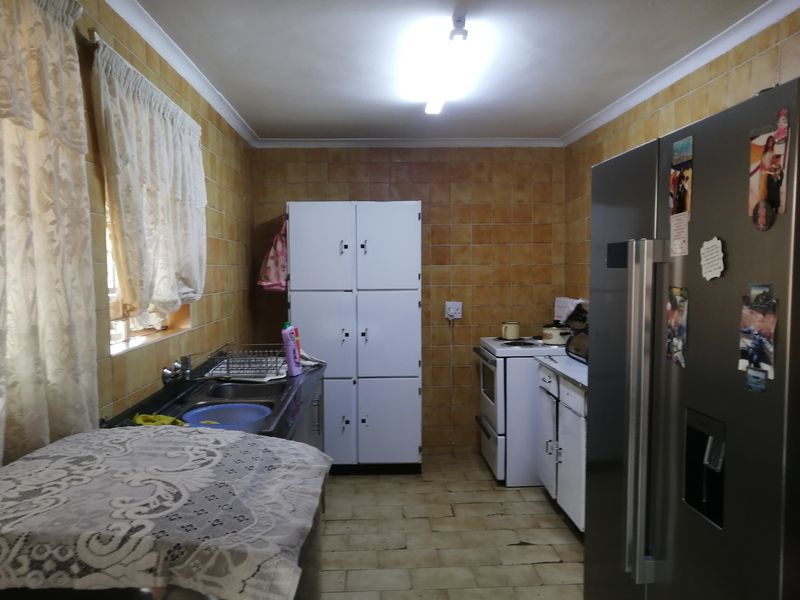 A functional kitchen featuring tiled walls and flooring, equipped with a double sink and built-in cabinetry, offering potential for a modern renovation.