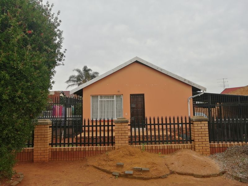 Front elevation of a single-story house featuring a brick perimeter wall, security fencing, and security bars on windows, set on a residential plot.