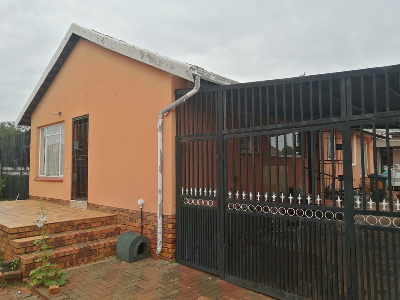 Front exterior view of the house featuring a paved driveway, metal security gate, and a small tiled entrance patio.