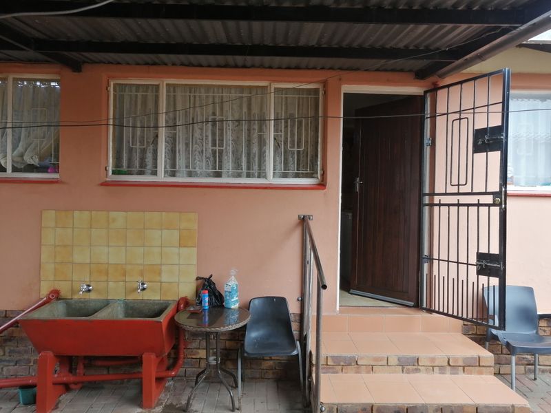 Covered outdoor patio area featuring a double concrete laundry sink, tiled steps, and a secure metal entrance gate.