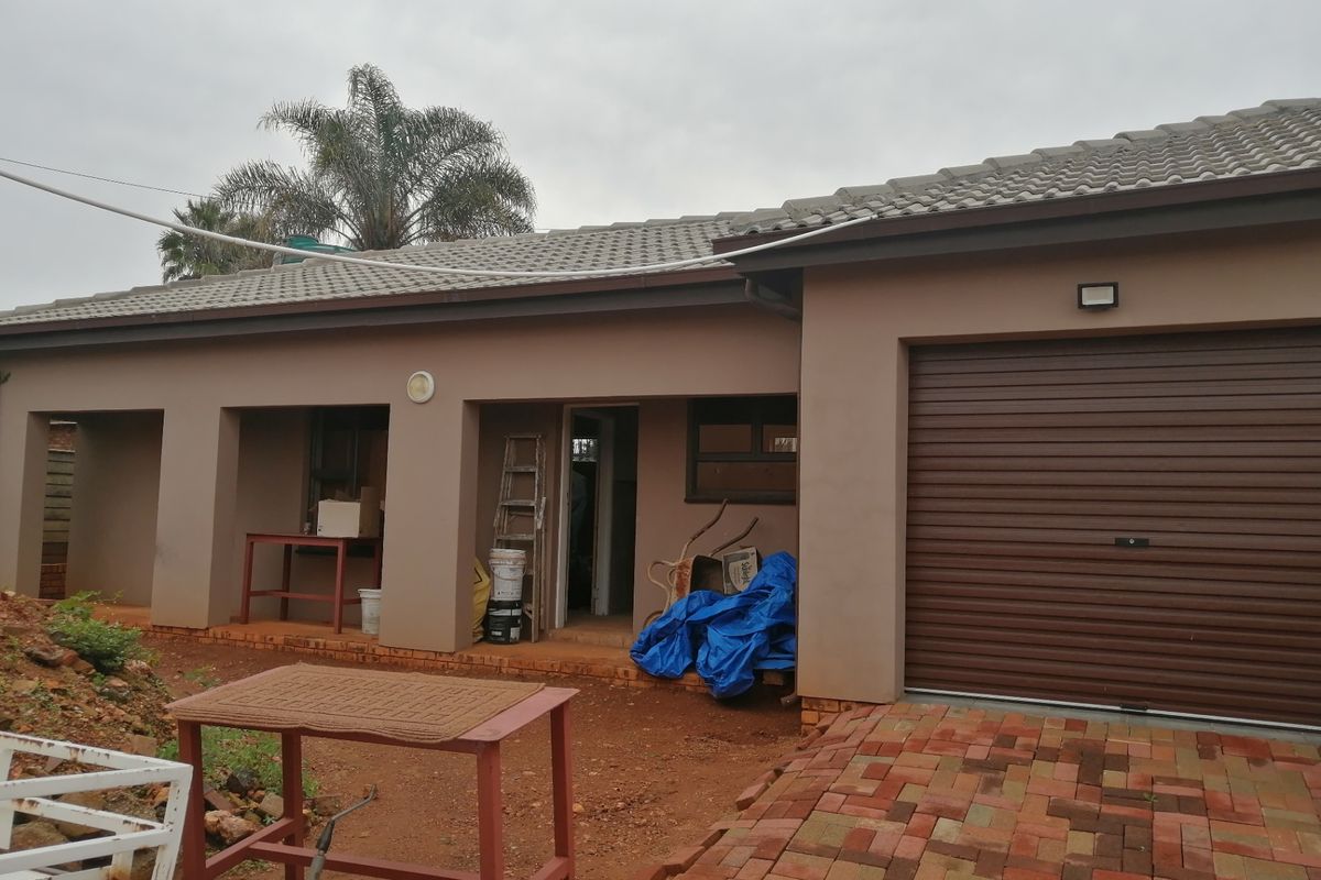Rear view of the property featuring a covered patio area, a single roller garage door, and unfinished brick paving in the yard.