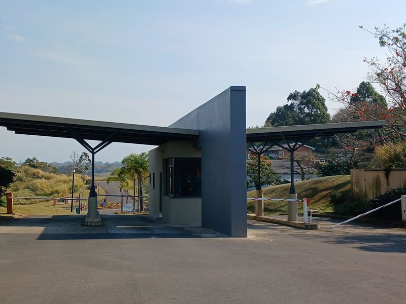 A modern security gatehouse entrance featuring a central guard booth, cantilevered roof structures, and automated boom gates for controlled access.