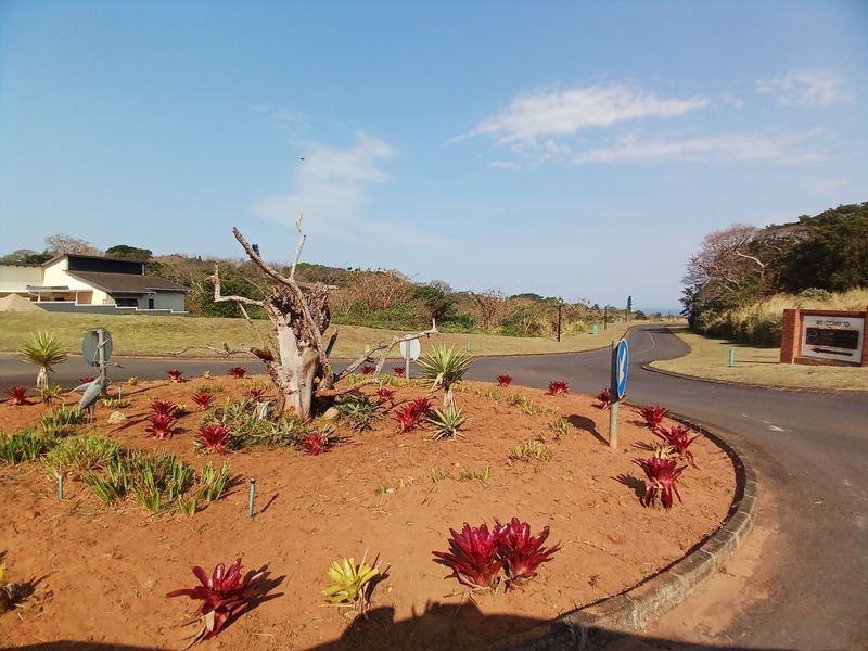 A view of the residential estate entrance featuring a landscaped roundabout with established plantings and paved access roads.