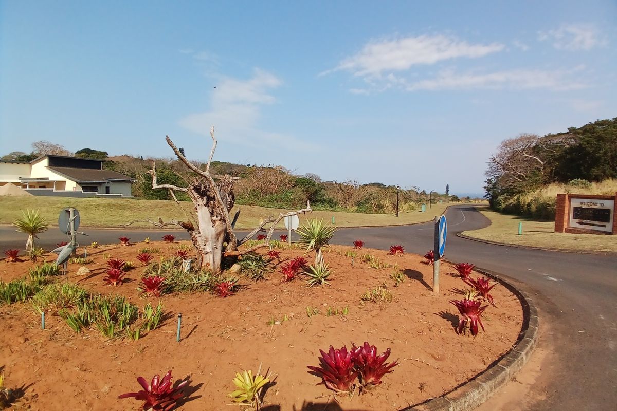 A view of the residential estate entrance featuring a landscaped roundabout with established plantings and paved access roads.