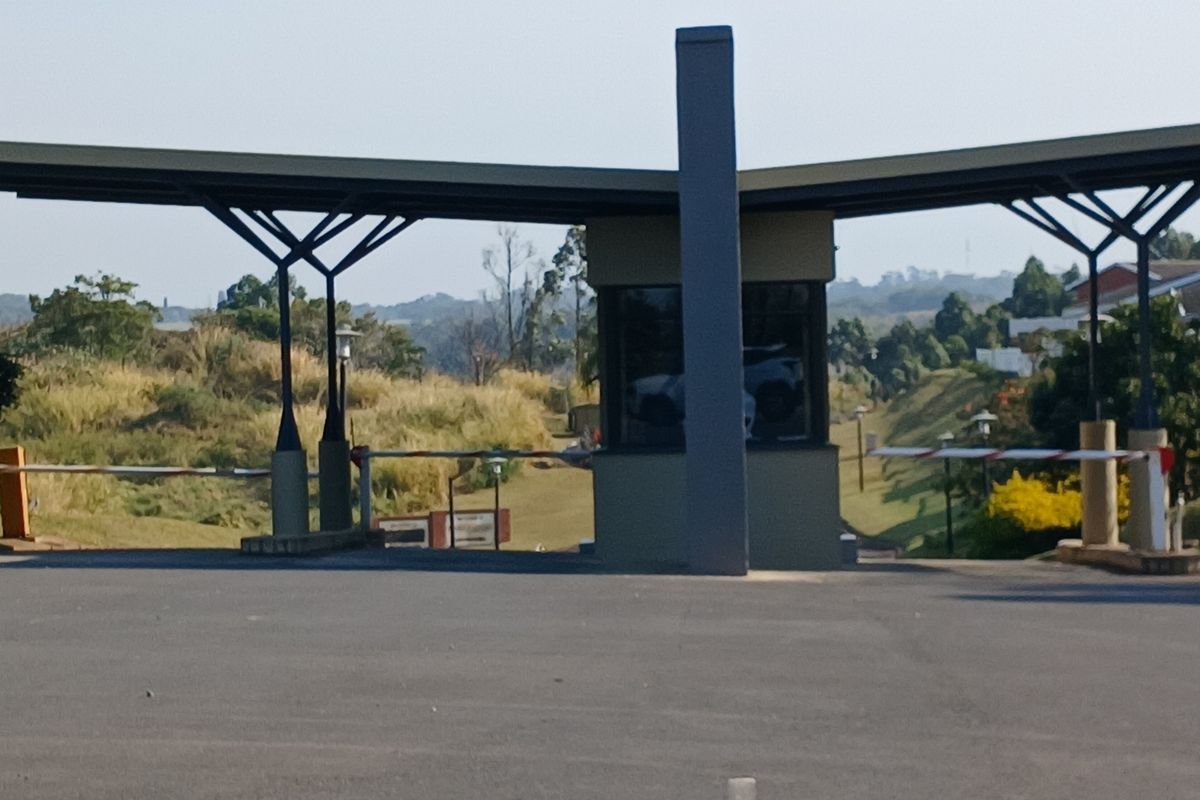 A view of the secure gated entrance and guardhouse for the residential estate, featuring a modern canopy structure and boom gate access control.