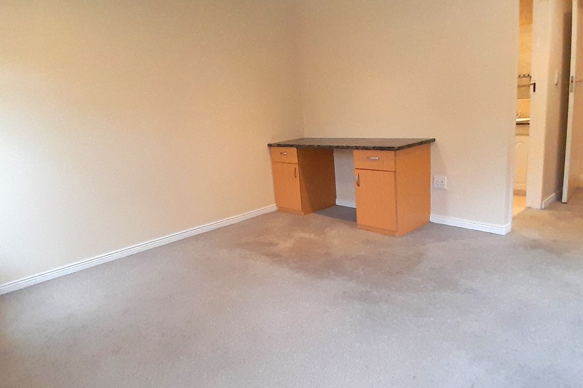 A vacant bedroom featuring neutral walls, carpet flooring, recessed lighting, and a built-in desk unit, with an adjacent view into a bathroom.