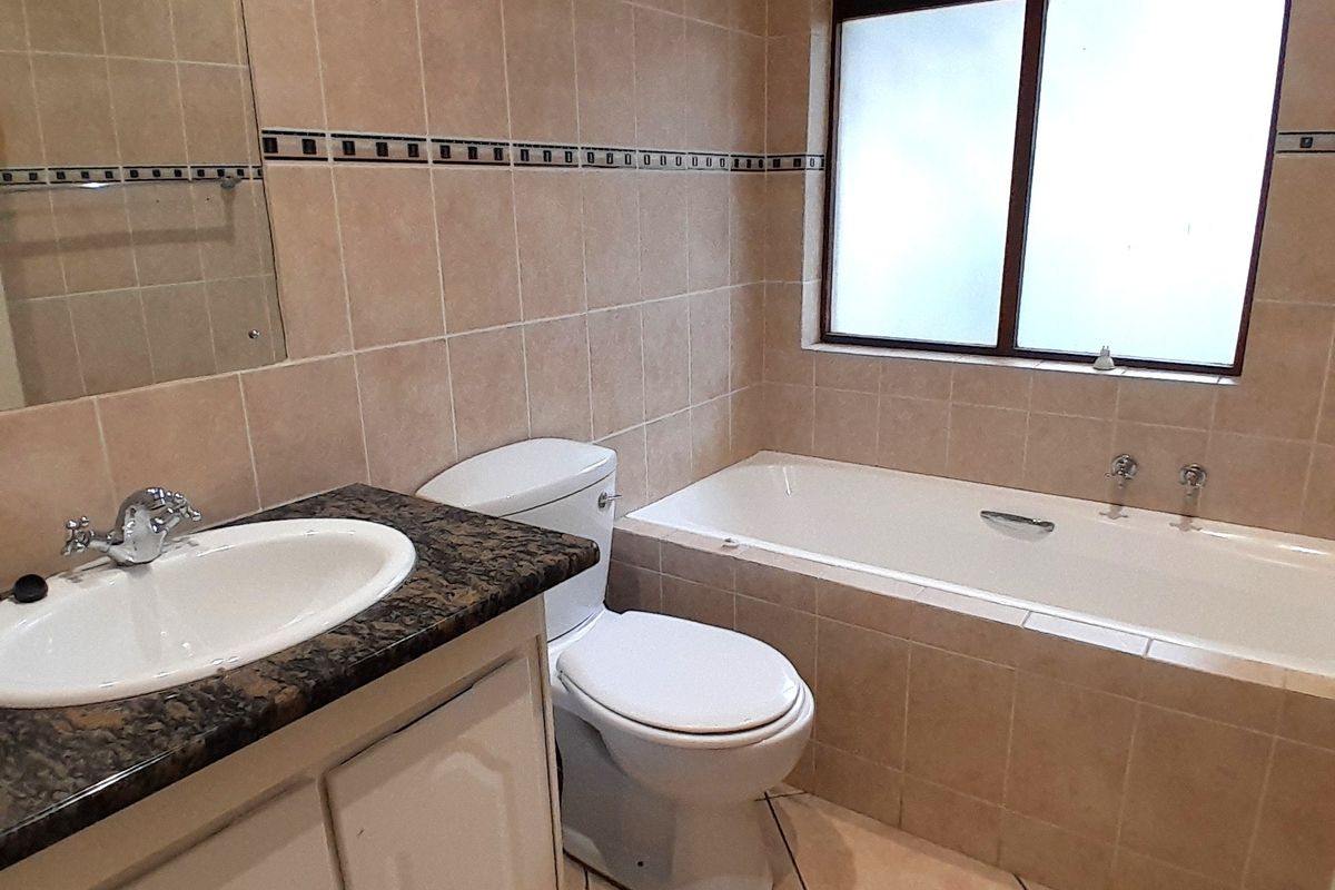 A functional bathroom featuring a vanity with granite countertop, built-in bathtub, and neutral wall tiling.