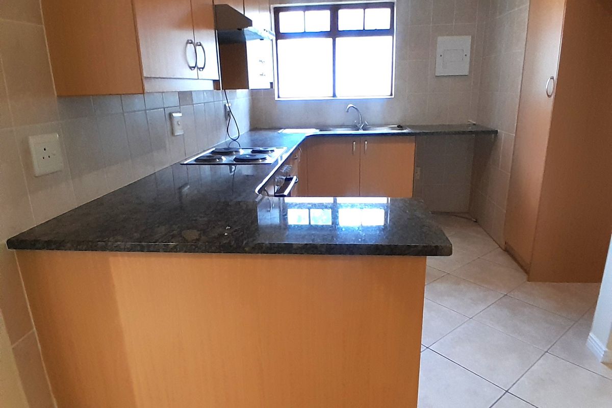 A functional kitchen featuring laminate cabinetry, granite countertops, an integrated electric hob with extractor fan, and tiled finishes throughout.