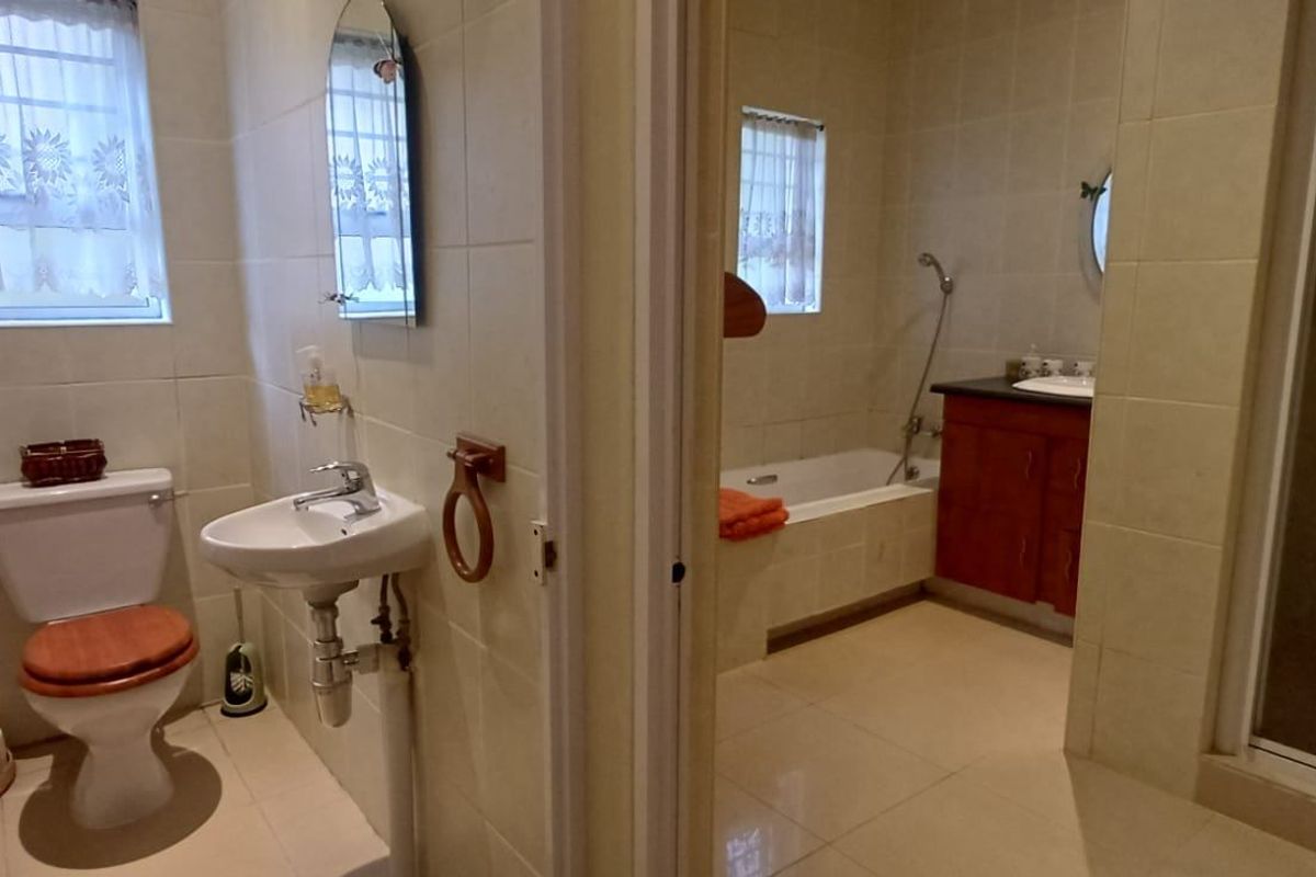 A functional bathroom featuring a separate shower, bathtub, pedestal basin, and toilet with neutral wall and floor tiling.