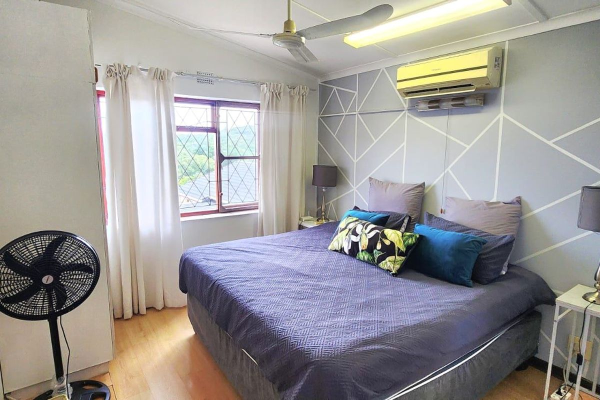 A bedroom featuring a split-system air conditioner, ceiling fan, built-in wardrobe, and laminate flooring with a decorative geometric wall finish.