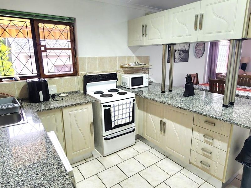 A functional kitchen featuring granite countertops, tiled flooring, and a breakfast bar, seamlessly connecting to the adjacent living and dining area.