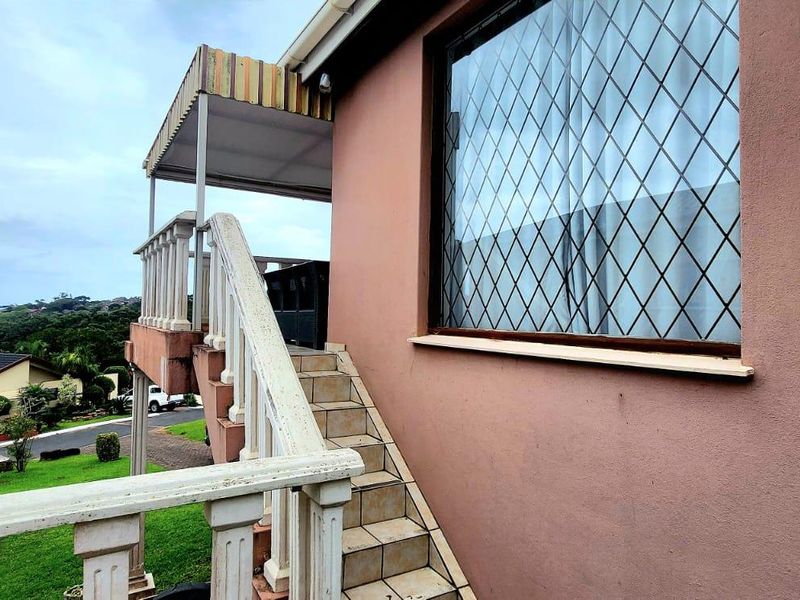 Exterior view of a townhouse featuring an external staircase leading to a covered landing, with security bars on the windows and coastal views.