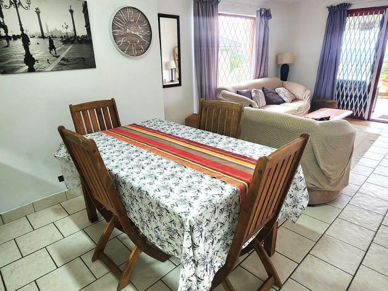 Open-plan living and dining area featuring ceramic floor tiles, granite kitchen surfaces, and direct access to an outdoor patio through a security gate.