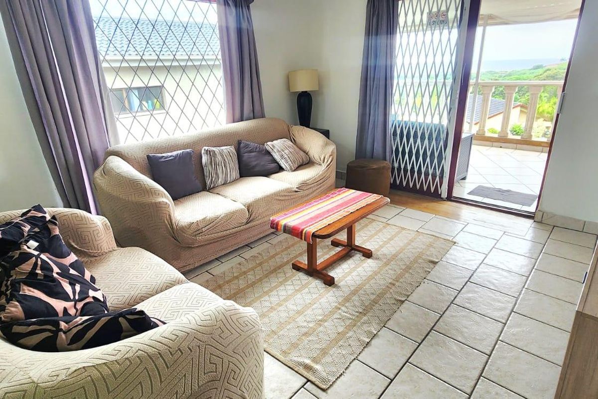 A living room featuring ceramic floor tiles, a security gate, and a sliding glass door providing access to an outdoor balcony area.
