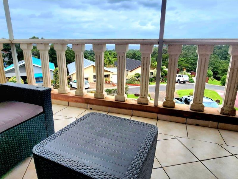Covered balcony featuring tiled flooring and a classic balustrade, offering elevated views of the surrounding neighborhood and greenery.