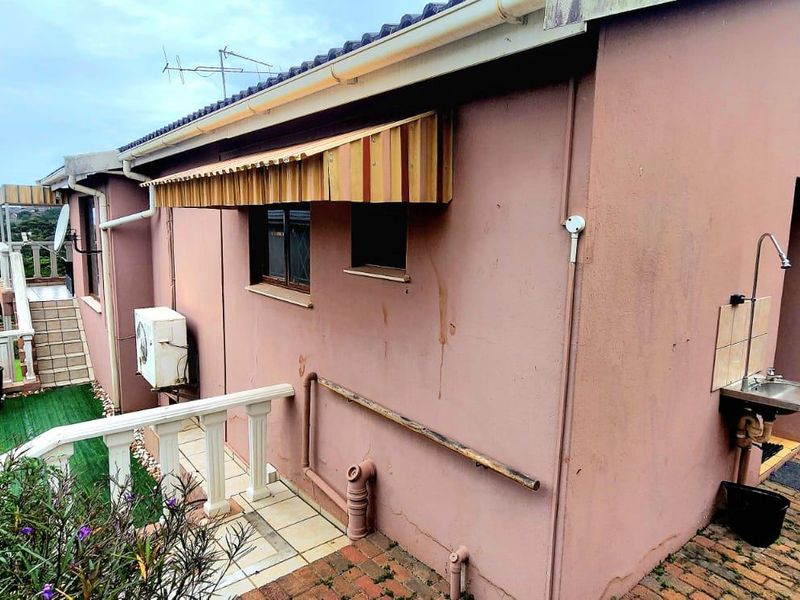 Rear exterior view of the townhouse featuring a paved area, external wash basin, and wall-mounted air conditioning unit.
