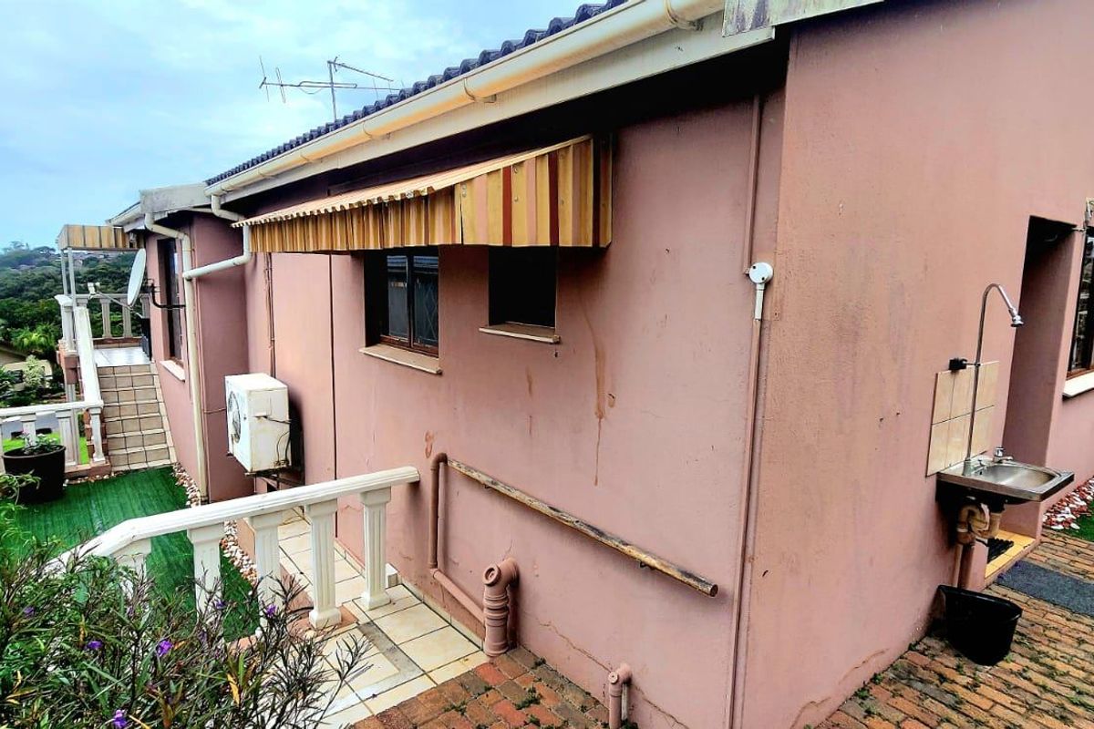 Rear exterior view of the townhouse featuring a paved area, external wash basin, and wall-mounted air conditioning unit.