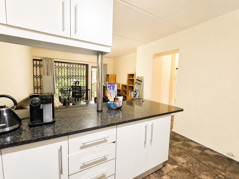 Open plan kitchen featuring granite countertops and white cabinetry, flowing into a living area with access to a secure patio.